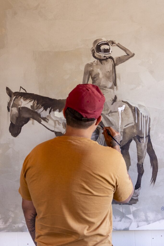 Image of a man painting a black and white picture of a person on a horse