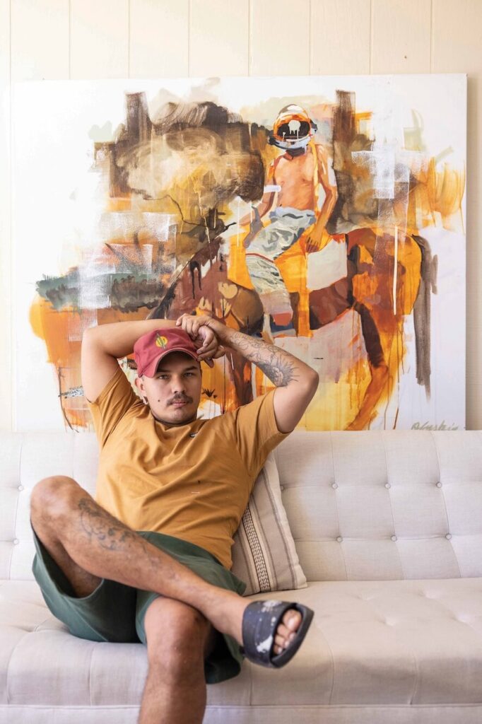 Image of an artist sitting in front of a painting posing