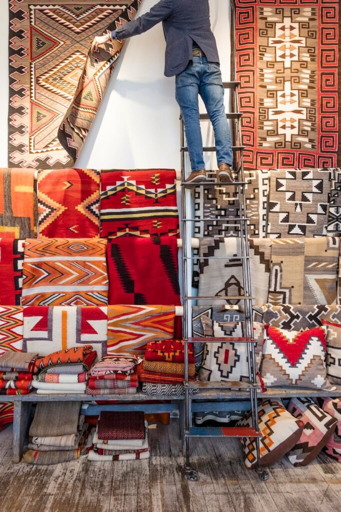 Image of a man on a ladder in front of beautifully designed New Mexican rugs